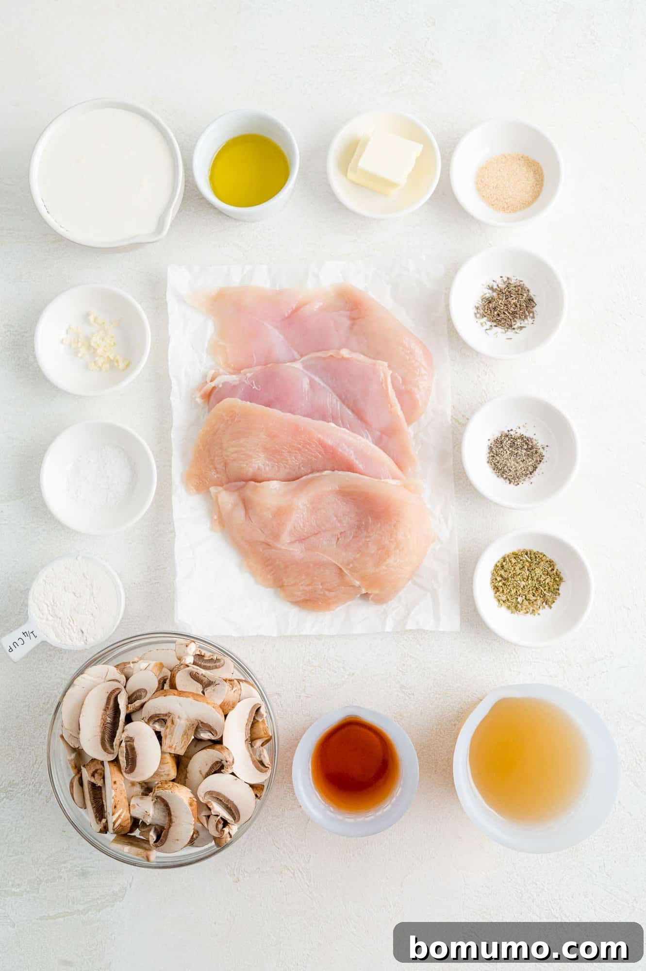 The array of fresh ingredients for making creamy chicken marsala, including chicken breasts, mushrooms, garlic, and herbs.
