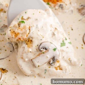 A spatula lifts a piece of chicken from a skillet of creamy chicken marsala, showcasing the rich sauce and tender meat.