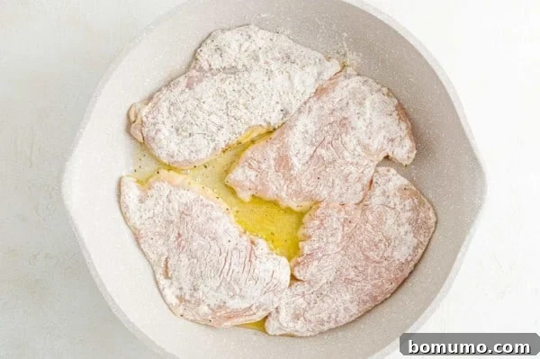 Lightly floured chicken cutlets sizzling in a hot skillet with oil, beginning to brown.