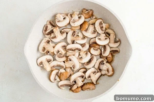 Freshly sliced mushrooms being added to a hot skillet, ready to be sautéed.