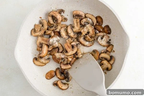 A spatula gently stirs sautéed mushrooms in a skillet, turning golden brown.