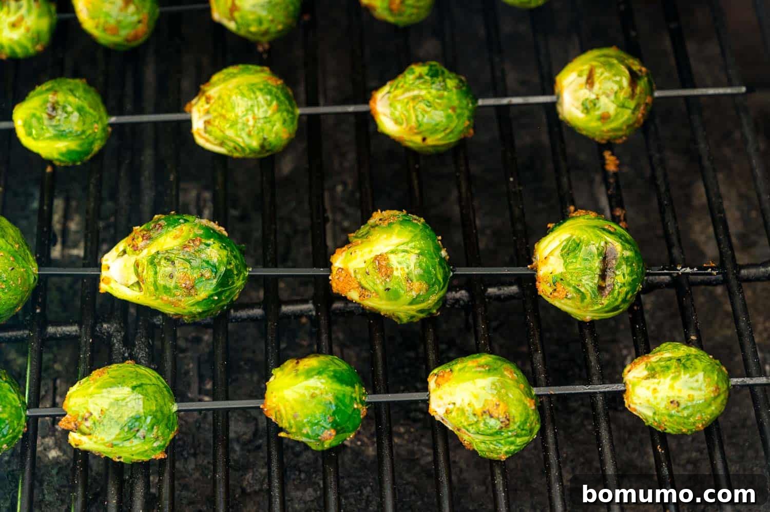 These are the best grilled Brussels sprouts! Cooked until golden and tossed in a combination of zesty lemon, parmesan, and fresh herbs. Close up of seasoned Brussels sprouts skewers on a grill.