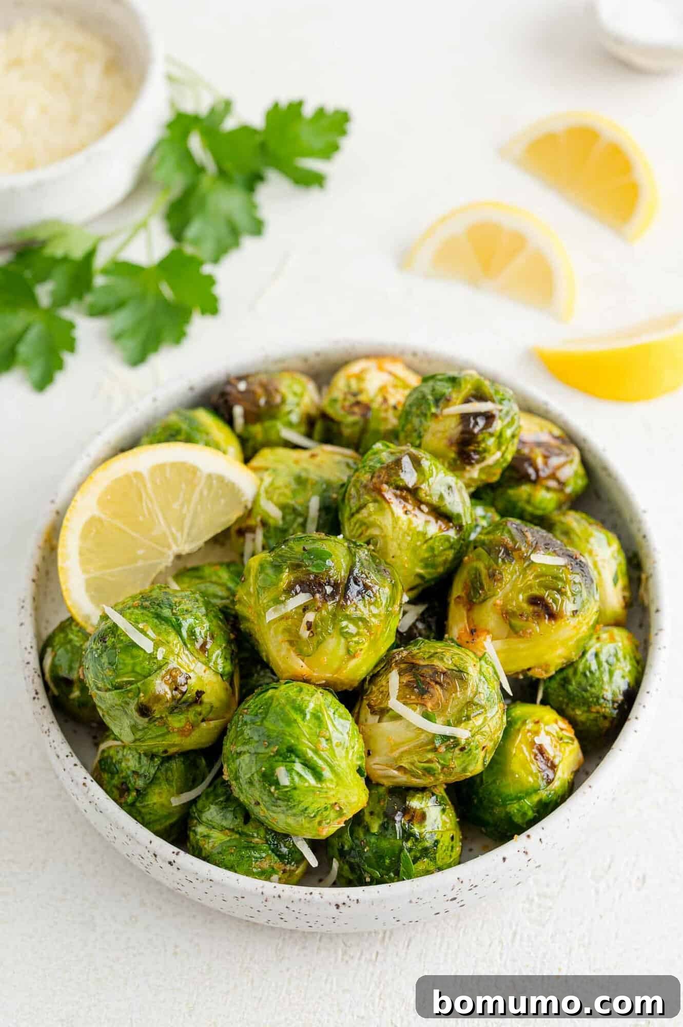 These are the best grilled Brussels sprouts! Cooked until golden and tossed in a combination of zesty lemon, parmesan, and fresh herbs. A bowl of grilled Brussels sprouts tossed in lemon and parmesan, garnished with lemon wedges.
