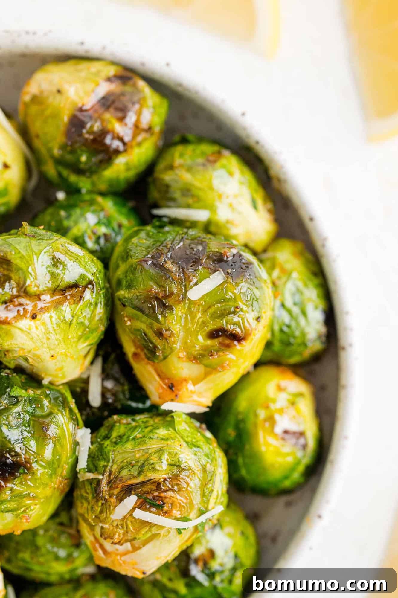 These are the best grilled Brussels sprouts! Cooked until golden and tossed in a combination of zesty lemon, parmesan, and fresh herbs. Close up overhead view of a bowl of grilled Brussels sprouts tossed in lemon and parmesan.