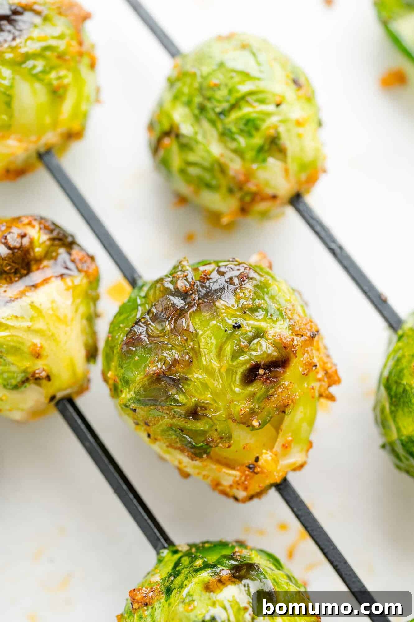 These are the best grilled Brussels sprouts! Cooked until golden and tossed in a combination of zesty lemon, parmesan, and fresh herbs. Close up of assorted grilled Brussels sprouts skewers.