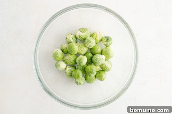 These are the best grilled Brussels sprouts! Cooked until golden and tossed in a combination of zesty lemon, parmesan, and fresh herbs. Uncooked Brussels sprouts in a glass bowl.