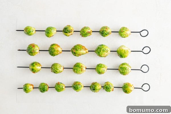 These are the best grilled Brussels sprouts! Cooked until golden and tossed in a combination of zesty lemon, parmesan, and fresh herbs. Overhead view of seasoned Brussels sprouts on four metal skewers.