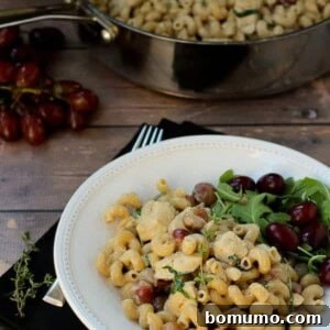 Pasta with grapes and chicken in a white bowl, ready to be served.