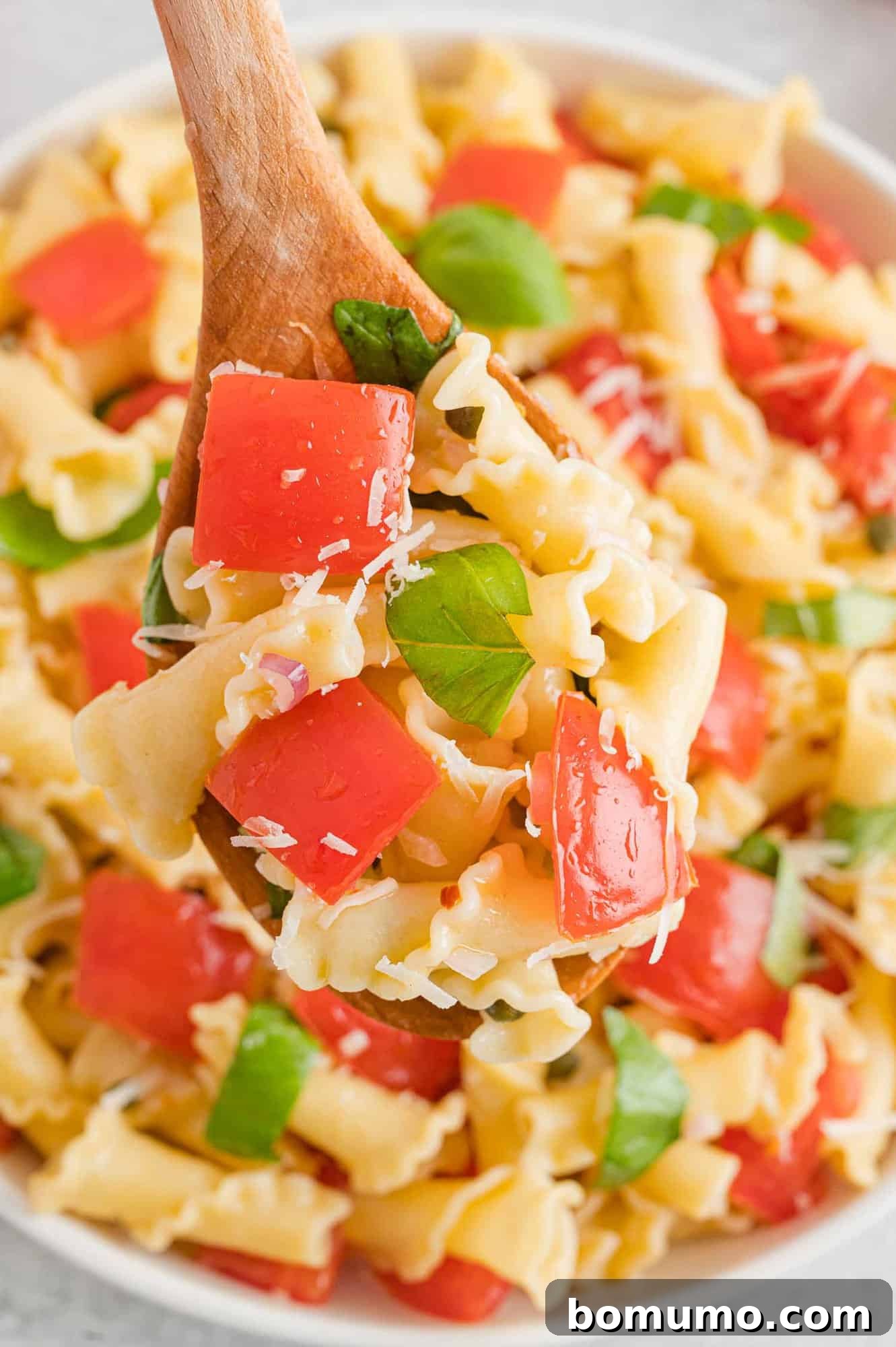 Close up of a wooden spoon scooping fresh tomato pasta from a large bowl.