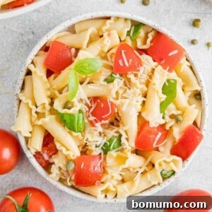 Overhead view of a bowl of fresh tomato pasta surrounded by scattered tomatoes.