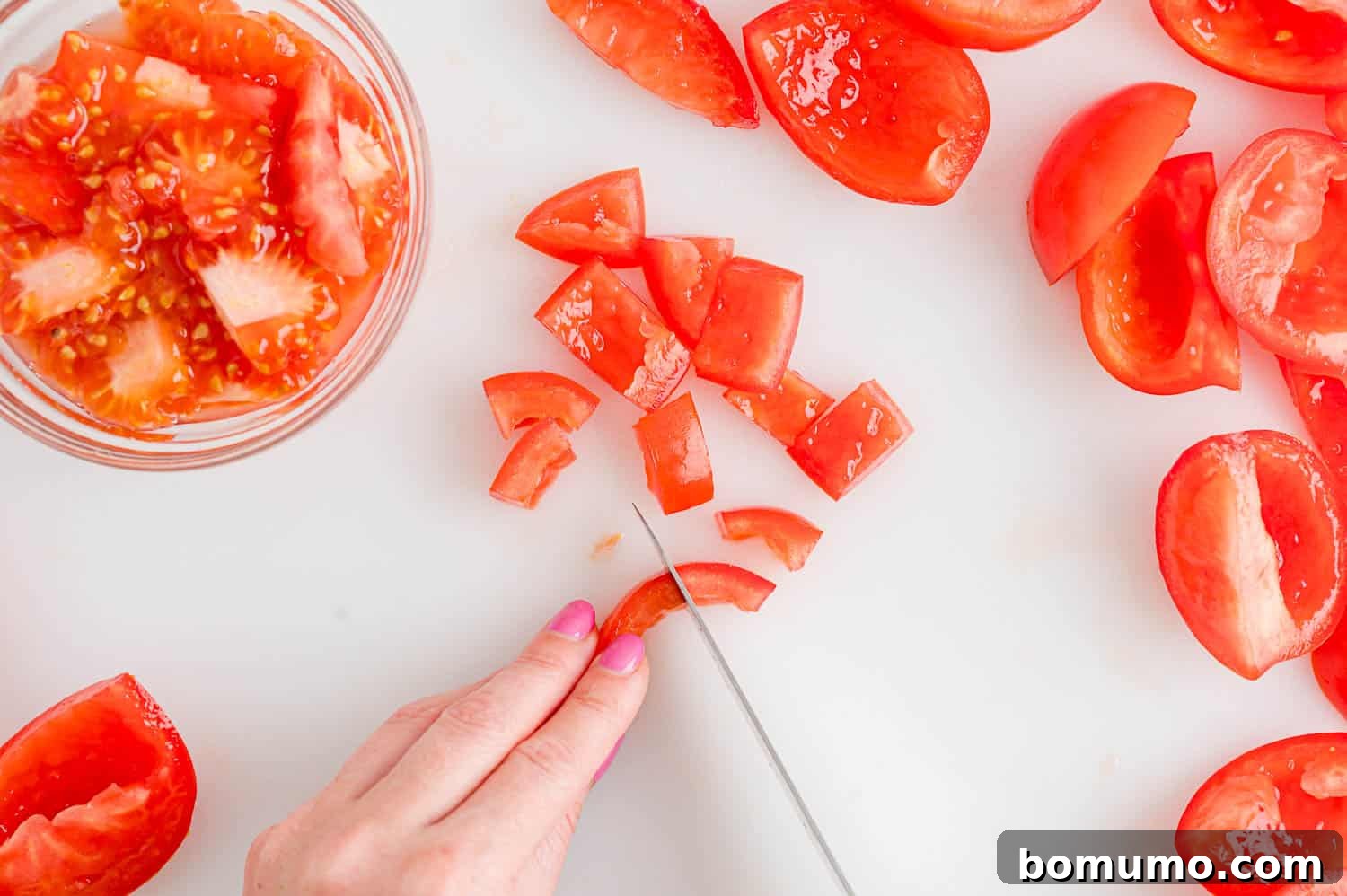 A hand using a knife to dice up deseeded and chopped fresh tomatoes.