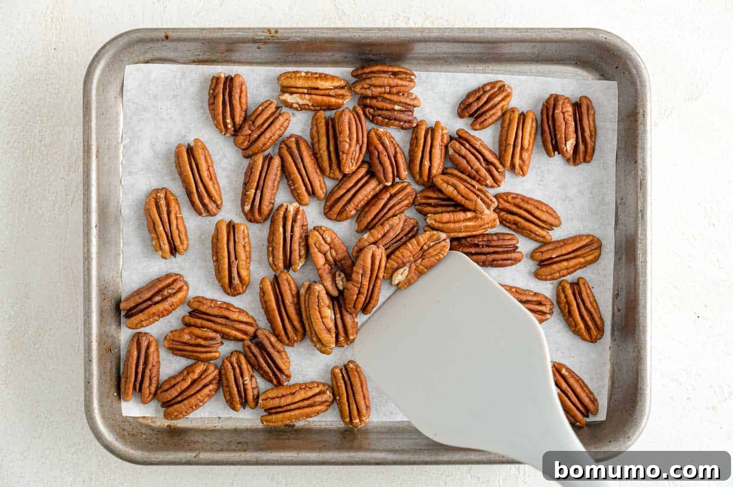 Pecan halves spread evenly on a baking sheet, actively toasting in the oven for a perfect golden finish.