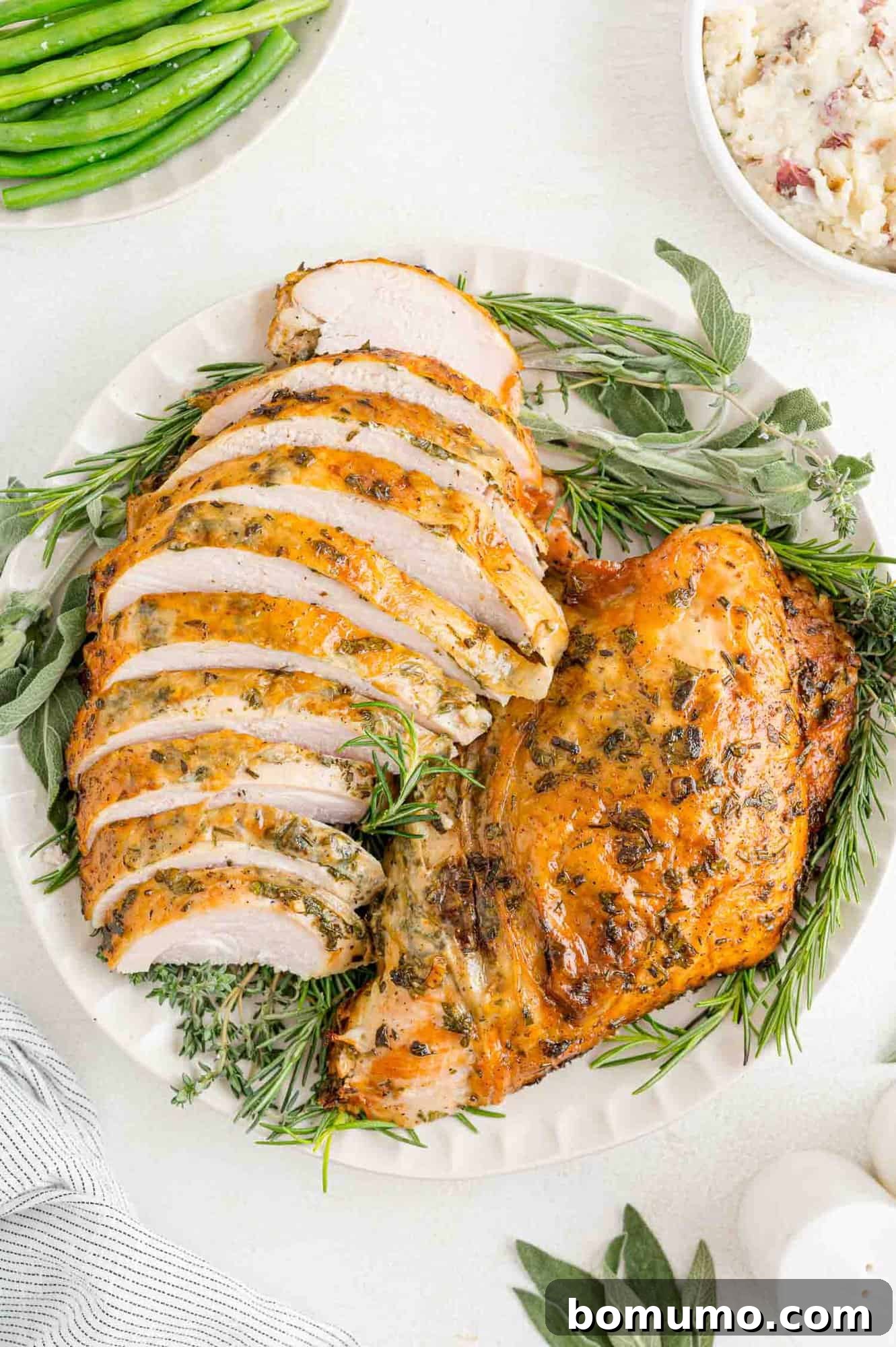 A beautifully golden-brown herb roasted turkey breast, perfectly sliced and arranged on a platter with fresh herbs for garnish.