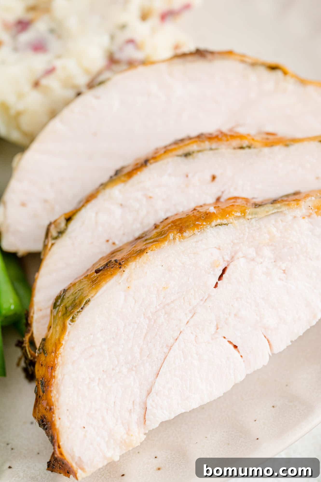 Three perfectly carved, juicy slices of herb roasted turkey breast, glistening and ready to be served.
