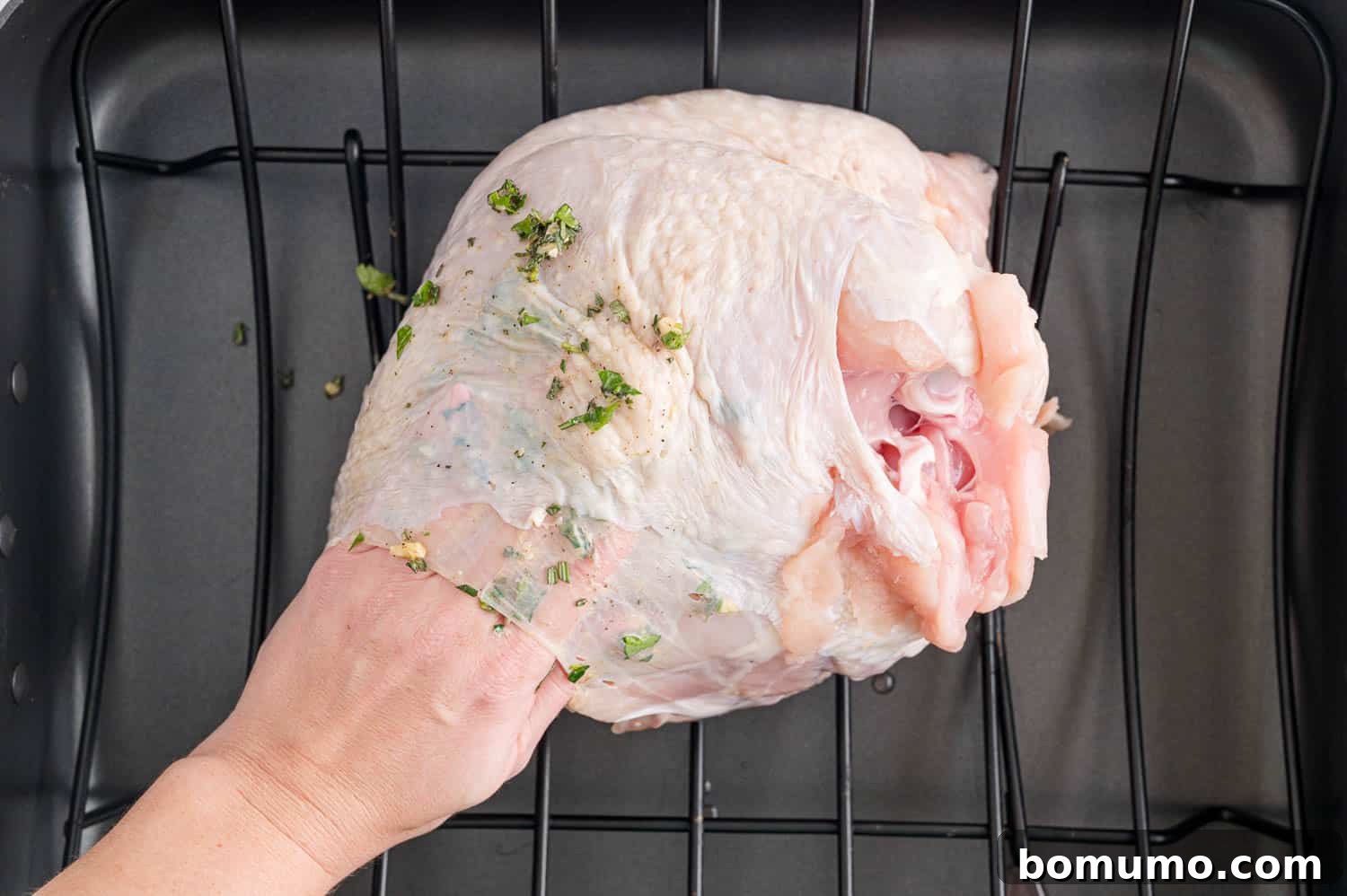 A raw turkey breast being gently lifted to allow the herb mixture to be applied directly under the skin, ensuring maximum flavor infusion.