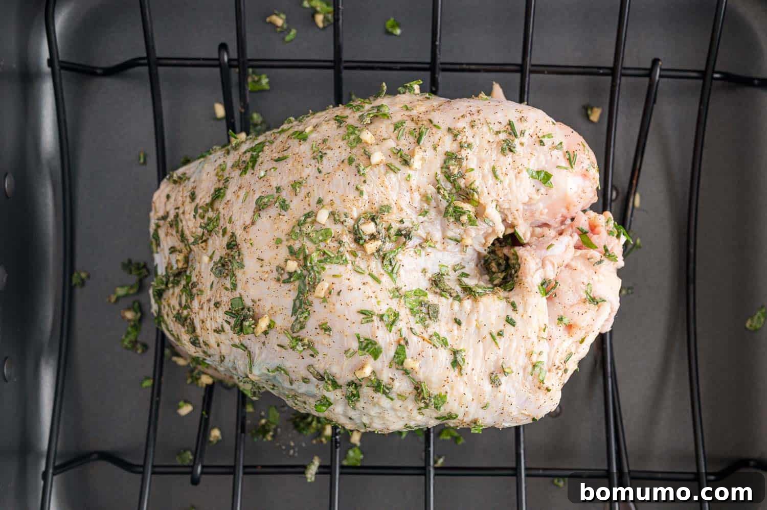 An uncooked turkey breast, now fully rubbed with the vibrant herb mixture both under and over the skin, showcasing a rich green and golden hue.