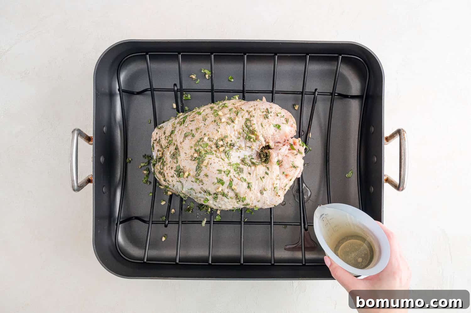 A steady stream of white wine being poured into the bottom of a roasting pan, surrounding a seasoned turkey breast on its rack.