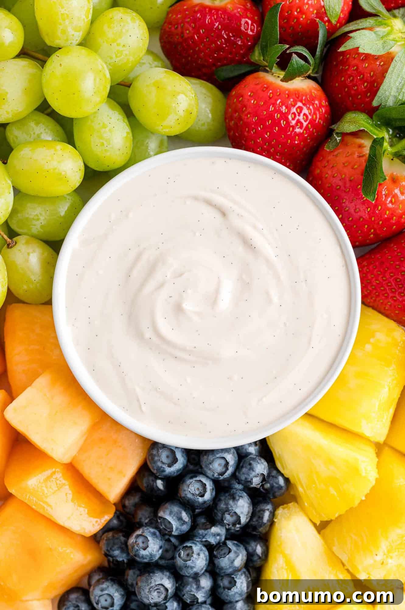 Overhead view of a bowl of cream cheese fruit dip in the center of a fruit platter with assorted fruits and berries.