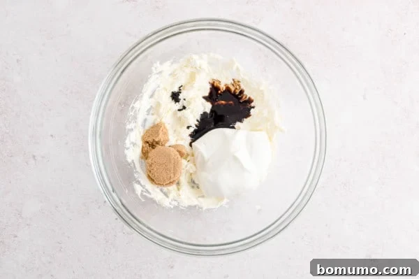 Ingredients for cream cheese fruit dip added to a mixing bowl with beaten cream cheese.