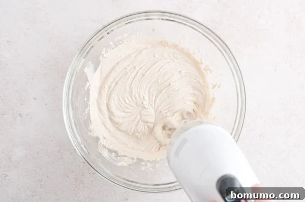 A hand mixer is used to combine the ingredients for fruit dip in a glass bowl.