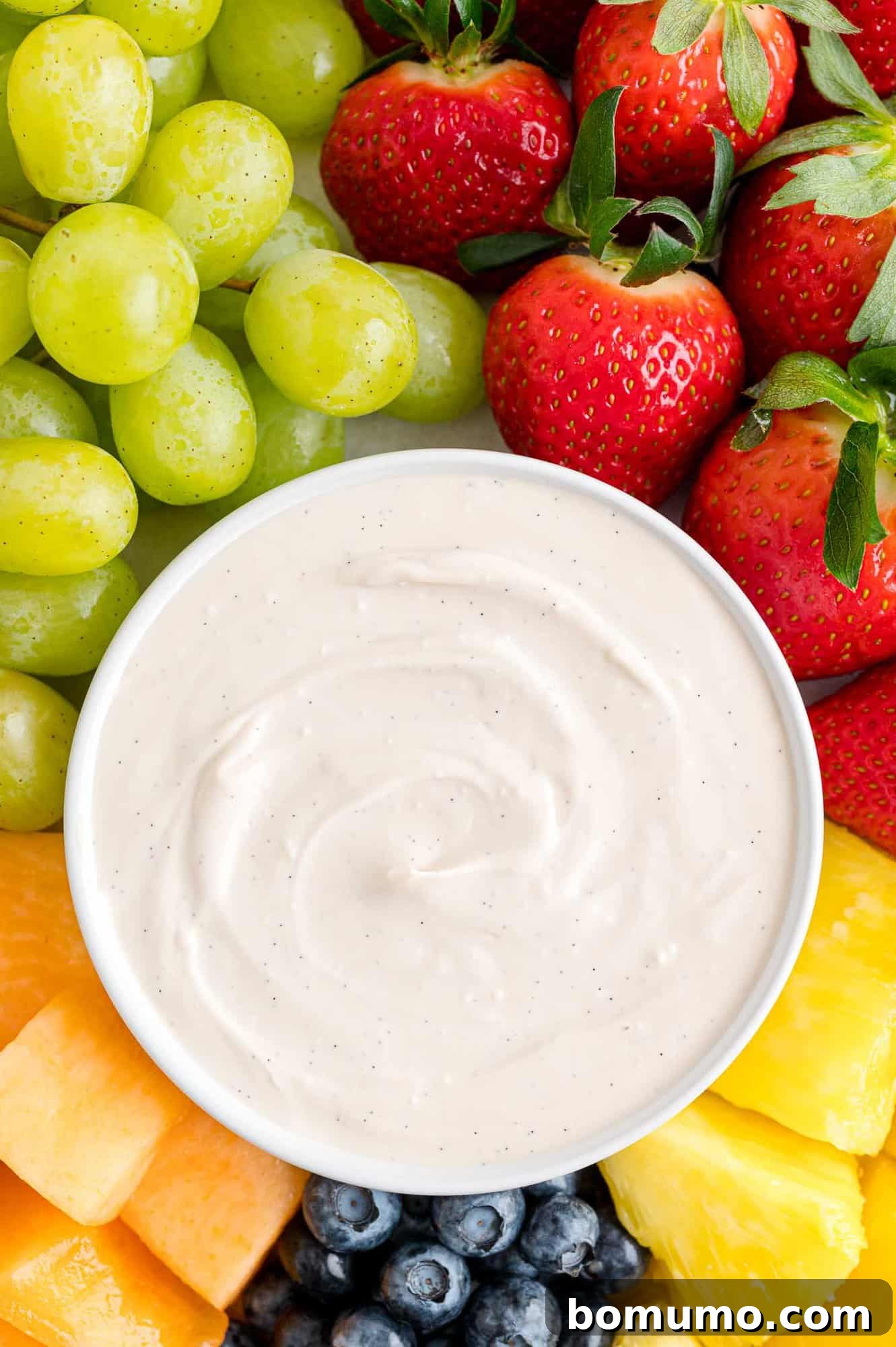 Overhead view of a bowl of cream cheese fruit dip in the center of a fruit platter with assorted fruits and berries.