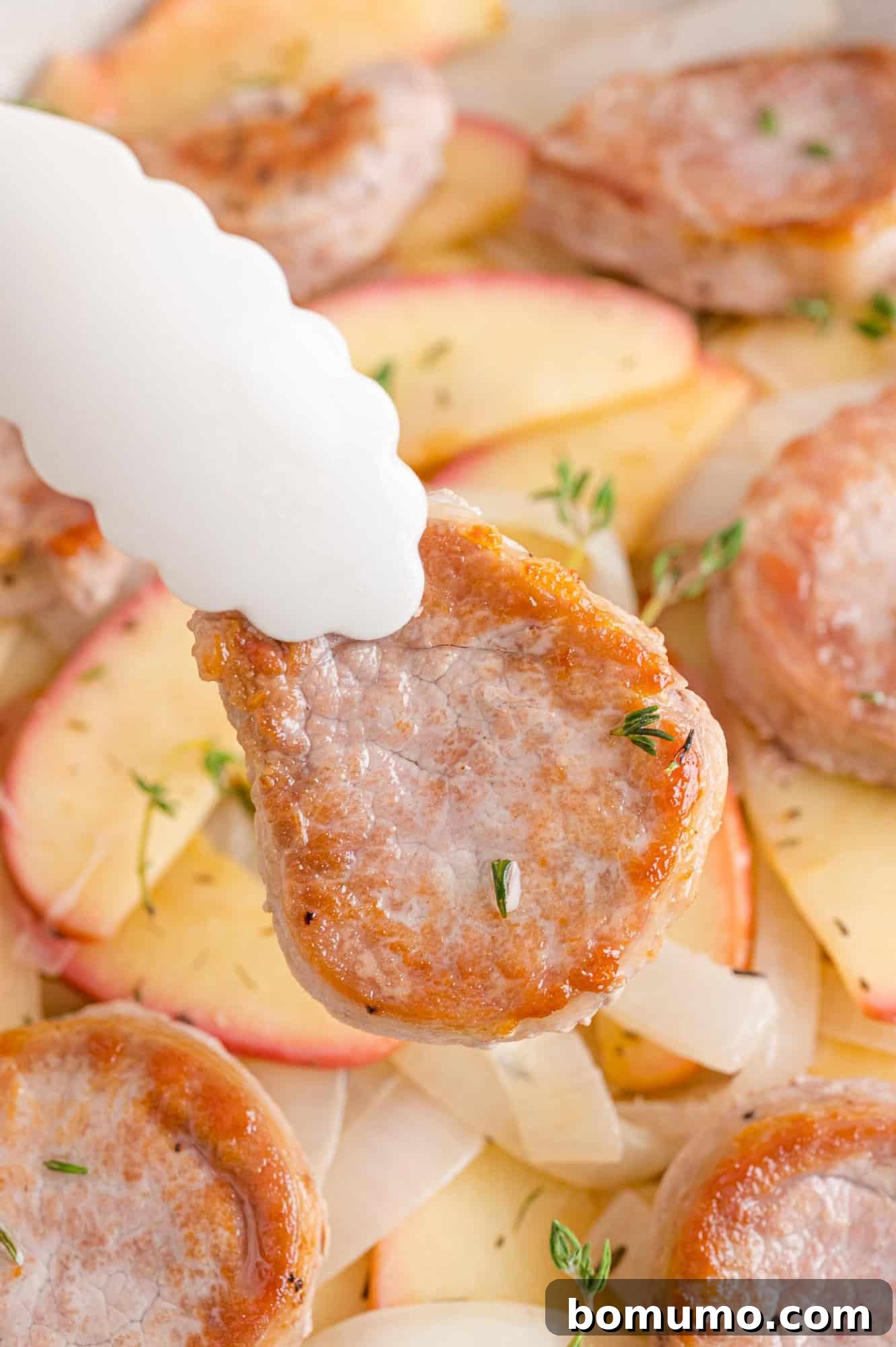 A glistening piece of uncooked pork tenderloin held by kitchen tongs, ready for seasoning and cooking.
