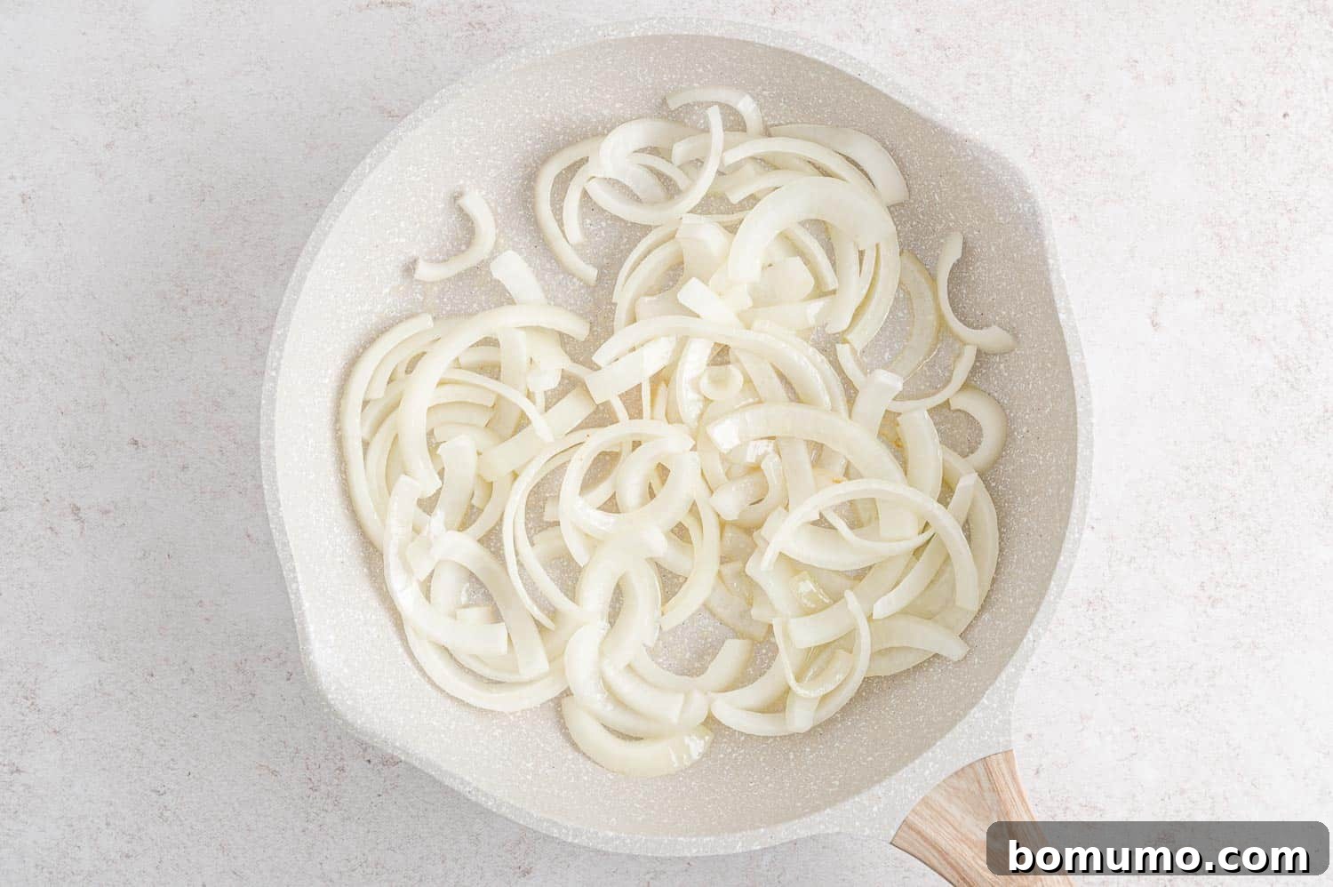 Thinly sliced onions sizzling gently in melted butter within a large frying pan, beginning to soften.
