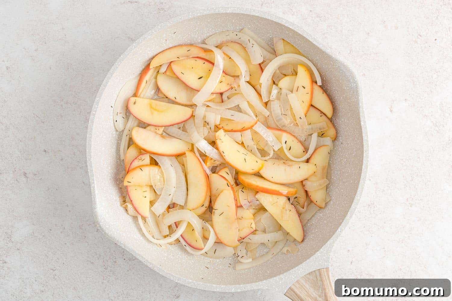 Caramelized apple and onion slices, glistening with butter and vinegar, resting in a frying pan after being seasoned.