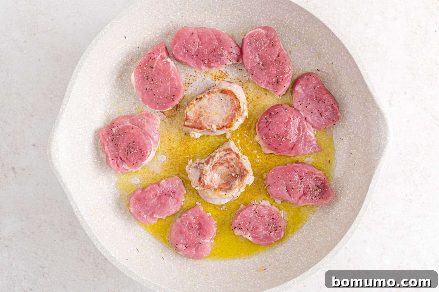 Several ½-inch thick slices of pork tenderloin searing to a golden brown in a hot skillet with olive oil.