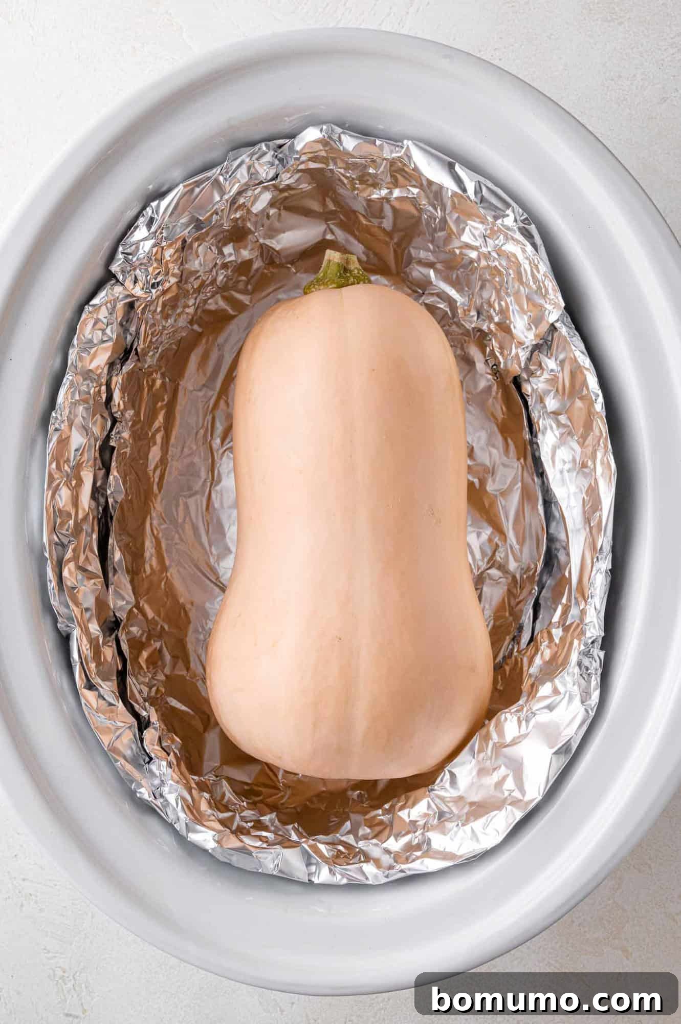 Whole butternut squash nestled in a foil-lined crockpot, ready to cook.