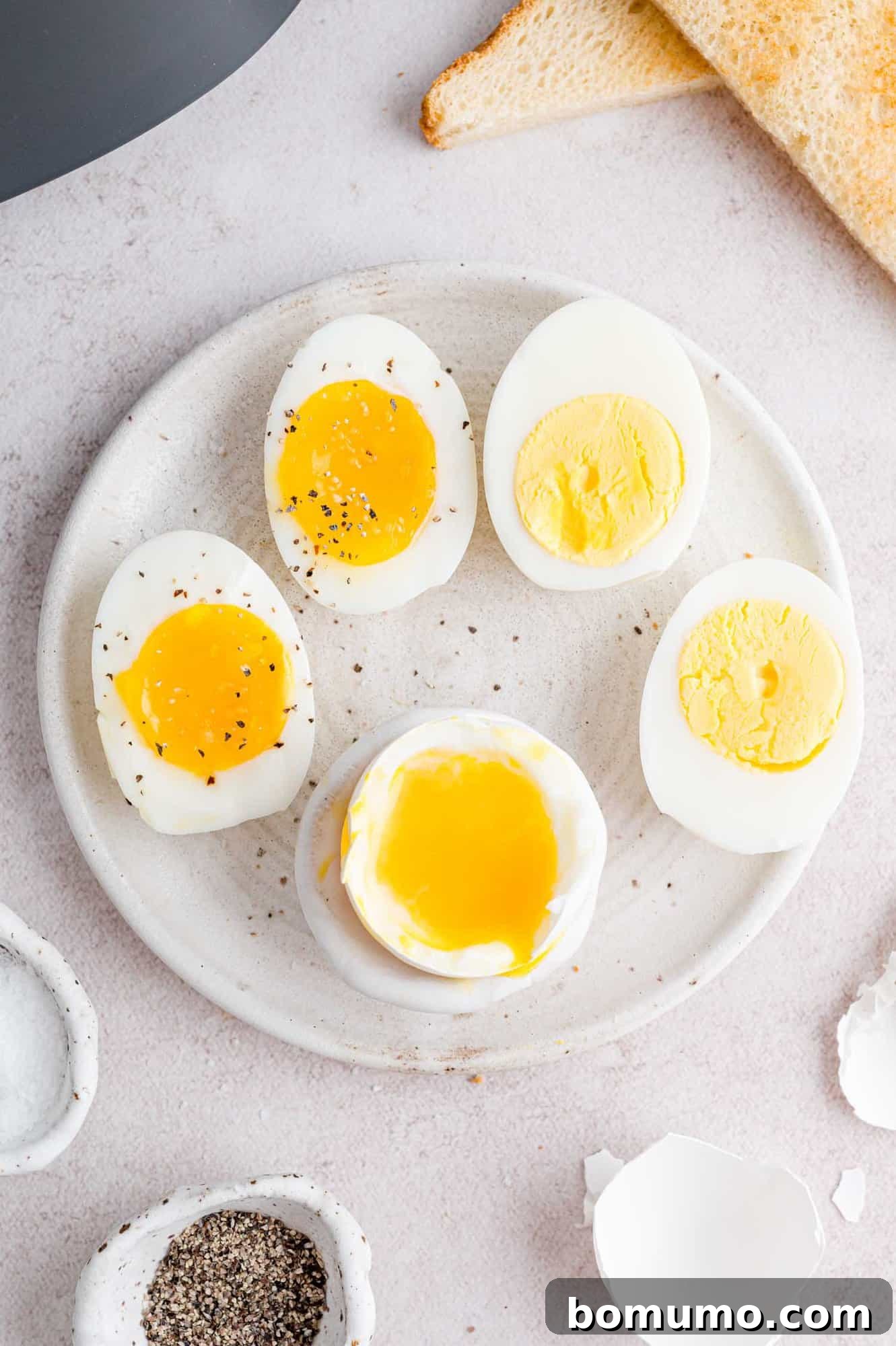 A close-up of beautifully seasoned air fryer boiled eggs on a plate, artfully sliced in half to display various levels of yolk doneness, from soft to hard. Ready to be served with a gourmet touch.