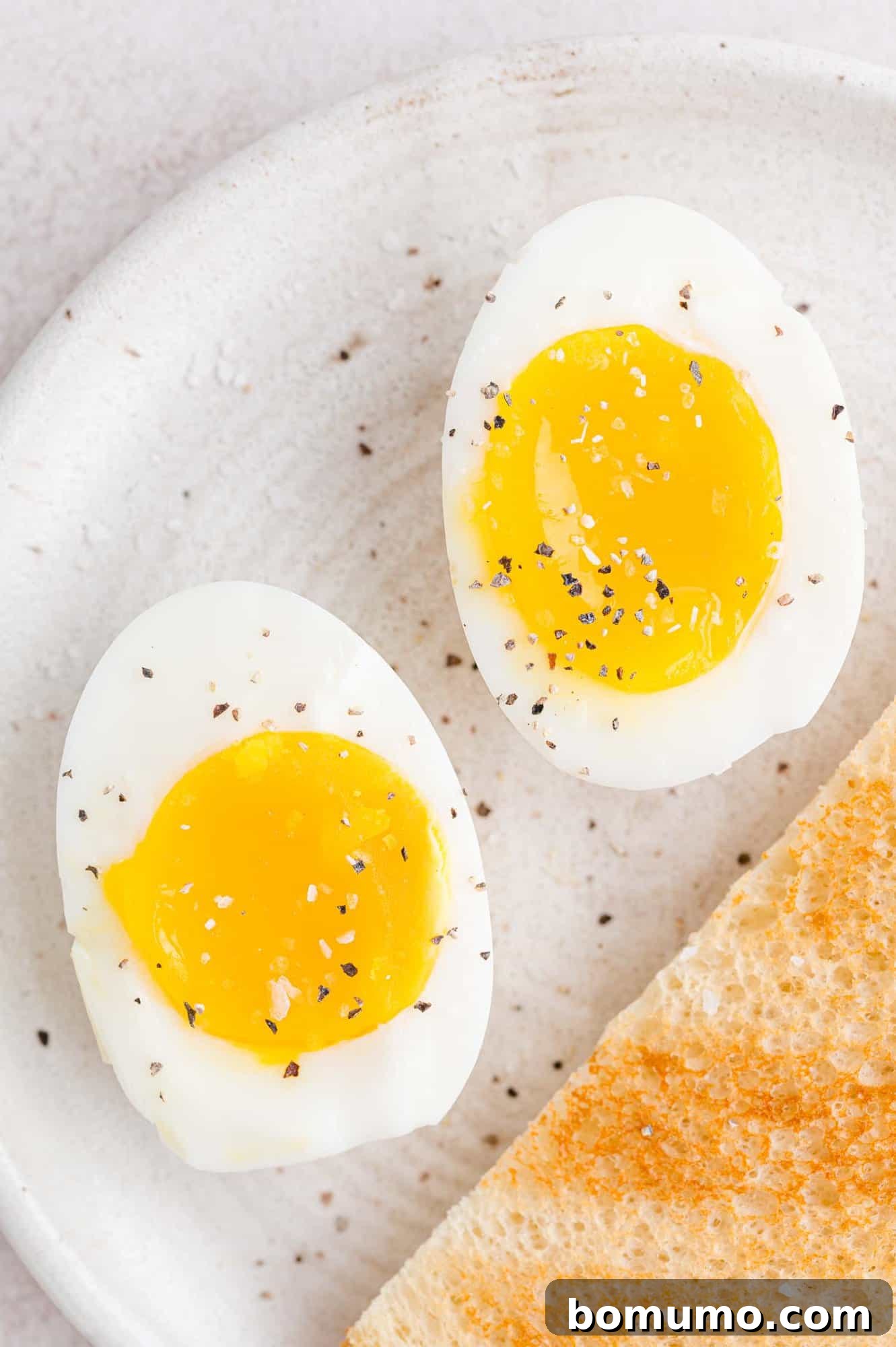 A close-up shot of two halves of a perfectly boiled egg on a plate, artfully seasoned with salt and pepper, presented alongside a slice of golden-brown toast. A simple, elegant, and wholesome meal.