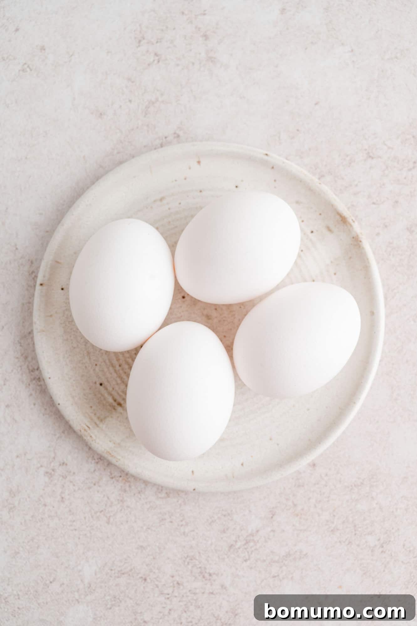 An elegant overhead shot displaying four perfectly cooked eggs, artfully arranged on a pristine white plate, awaiting their next delicious preparation or serving.