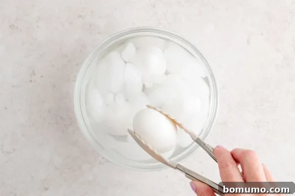 A hand gently lowers a freshly cooked, hot egg into a chilling bowl of ice water using tongs, demonstrating the essential step of immediate cooling after air frying.