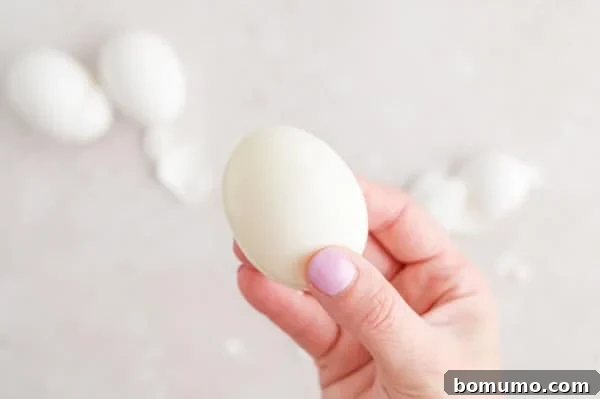 A hand proudly holds up a perfectly peeled, smooth boiled egg, showcasing the clean result achieved through the air frying and ice bath method.