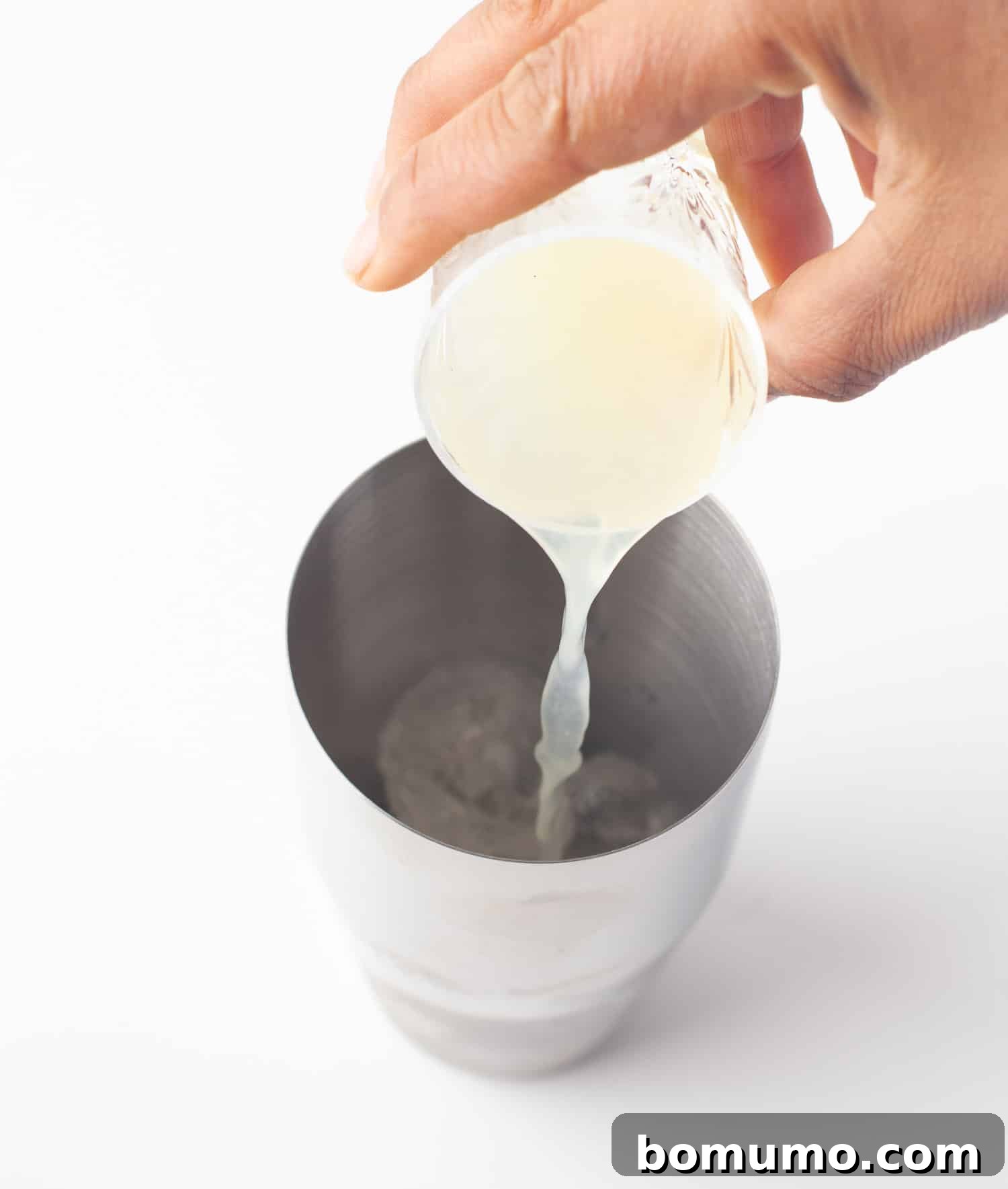 The vibrant pineapple juice being poured into a cocktail shaker, adding a tropical sweetness to the margarita base.