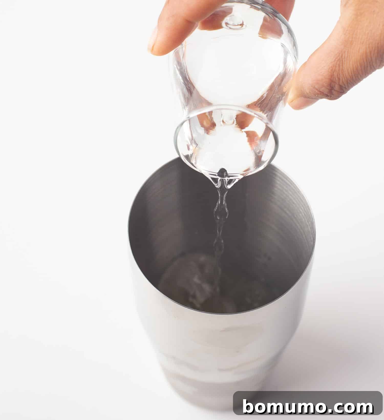 A stream of tequila being poured into a cocktail shaker, forming the alcoholic base for the pineapple margarita.
