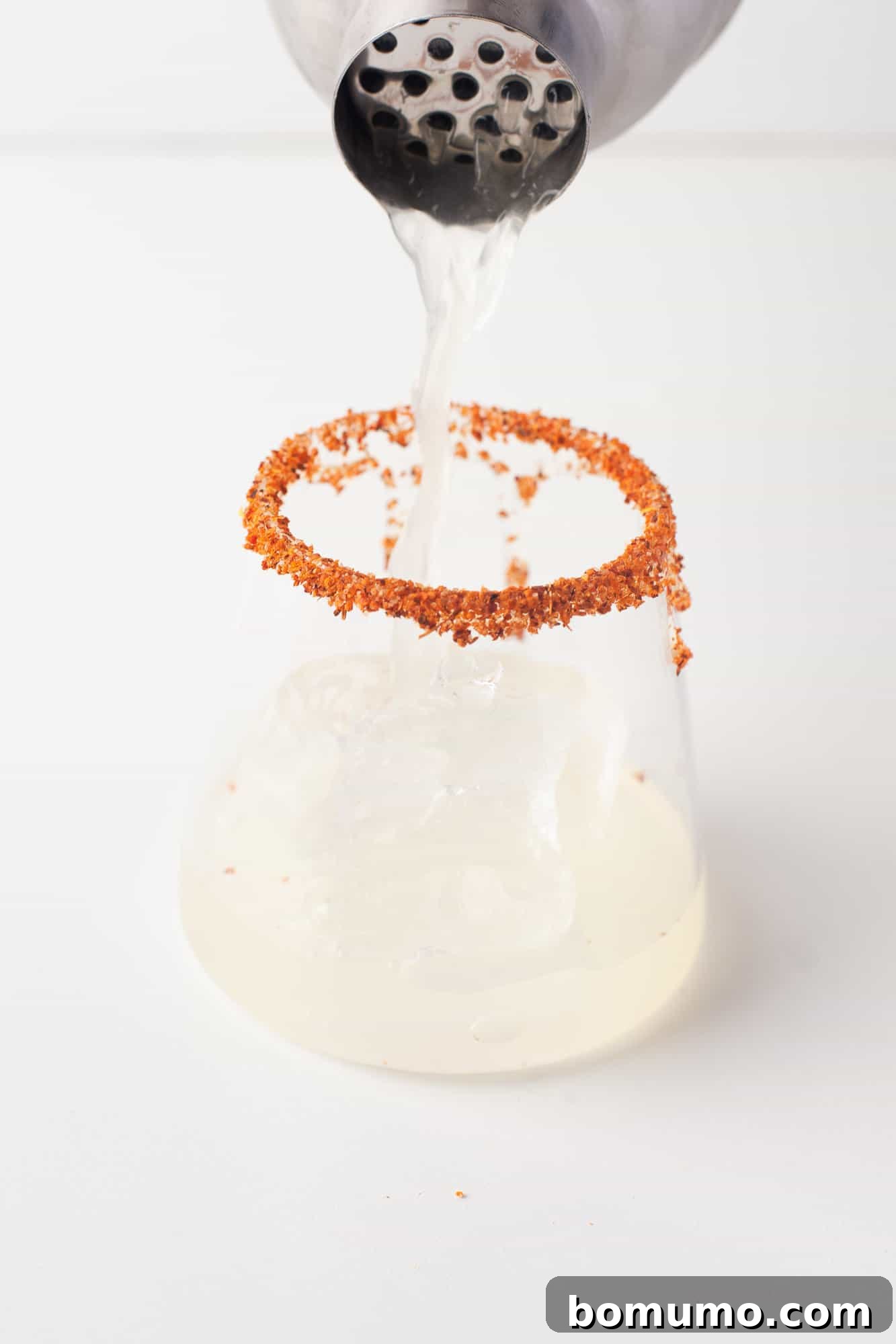 A refreshing pineapple margarita being poured from a cocktail shaker into a rimmed glass filled with ice, ready for enjoyment.