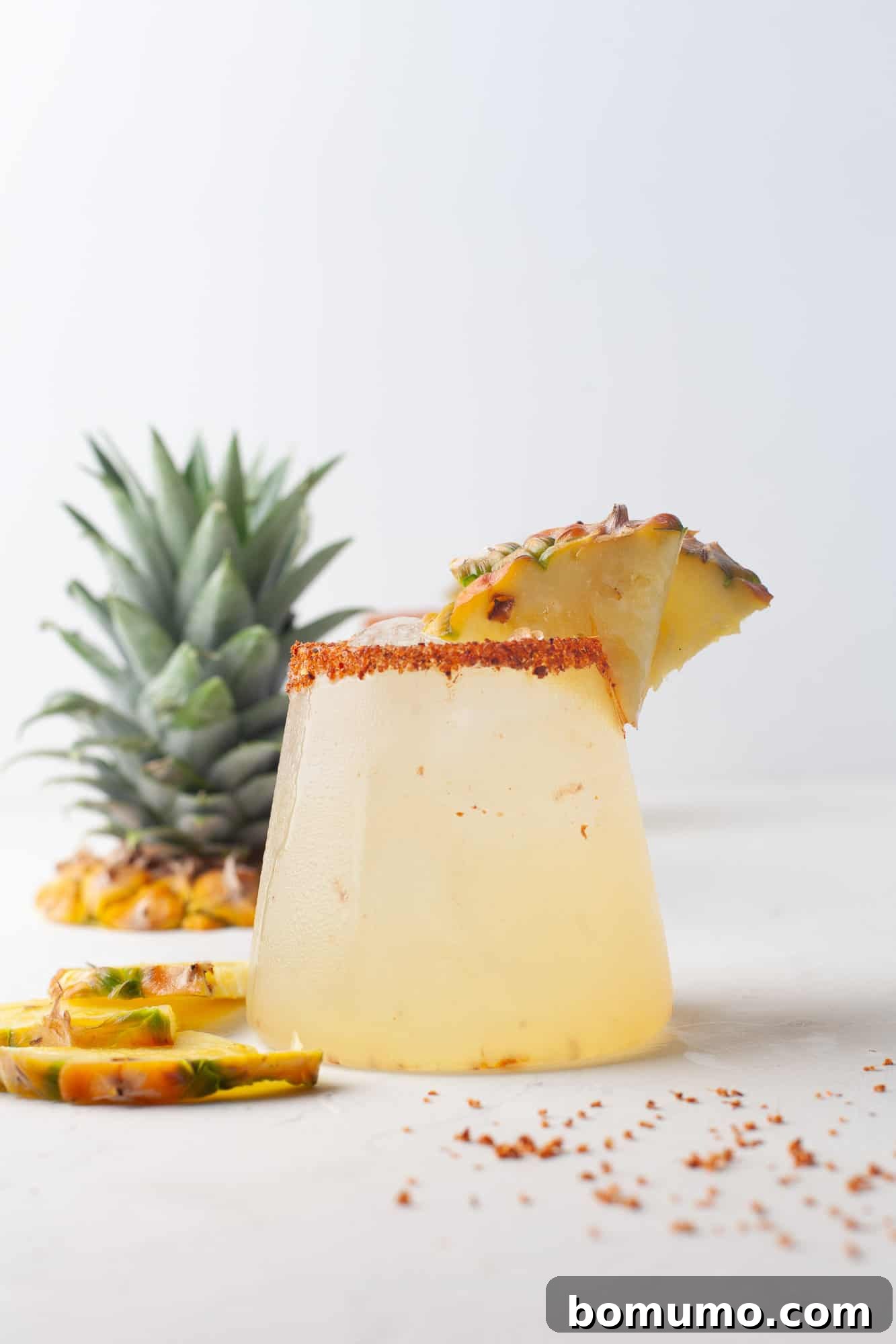 A beautifully presented pineapple margarita with a fresh pineapple top blurred in the background, emphasizing the tropical essence of the drink.