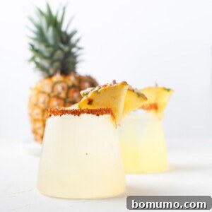 A vibrant pineapple margarita with a chili-spiced rim, ready to be enjoyed.