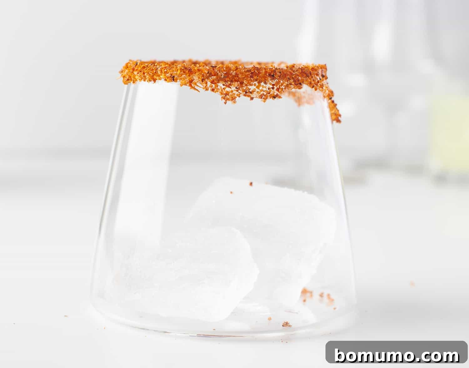An empty glass with a perfectly spiced rim, showcasing the colorful Tajín seasoning, ready to be filled with a refreshing pineapple margarita.