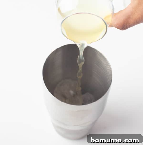 Various cocktail ingredients, including lime juice and agave syrup, being poured into a cocktail shaker filled with ice, ready for mixing.