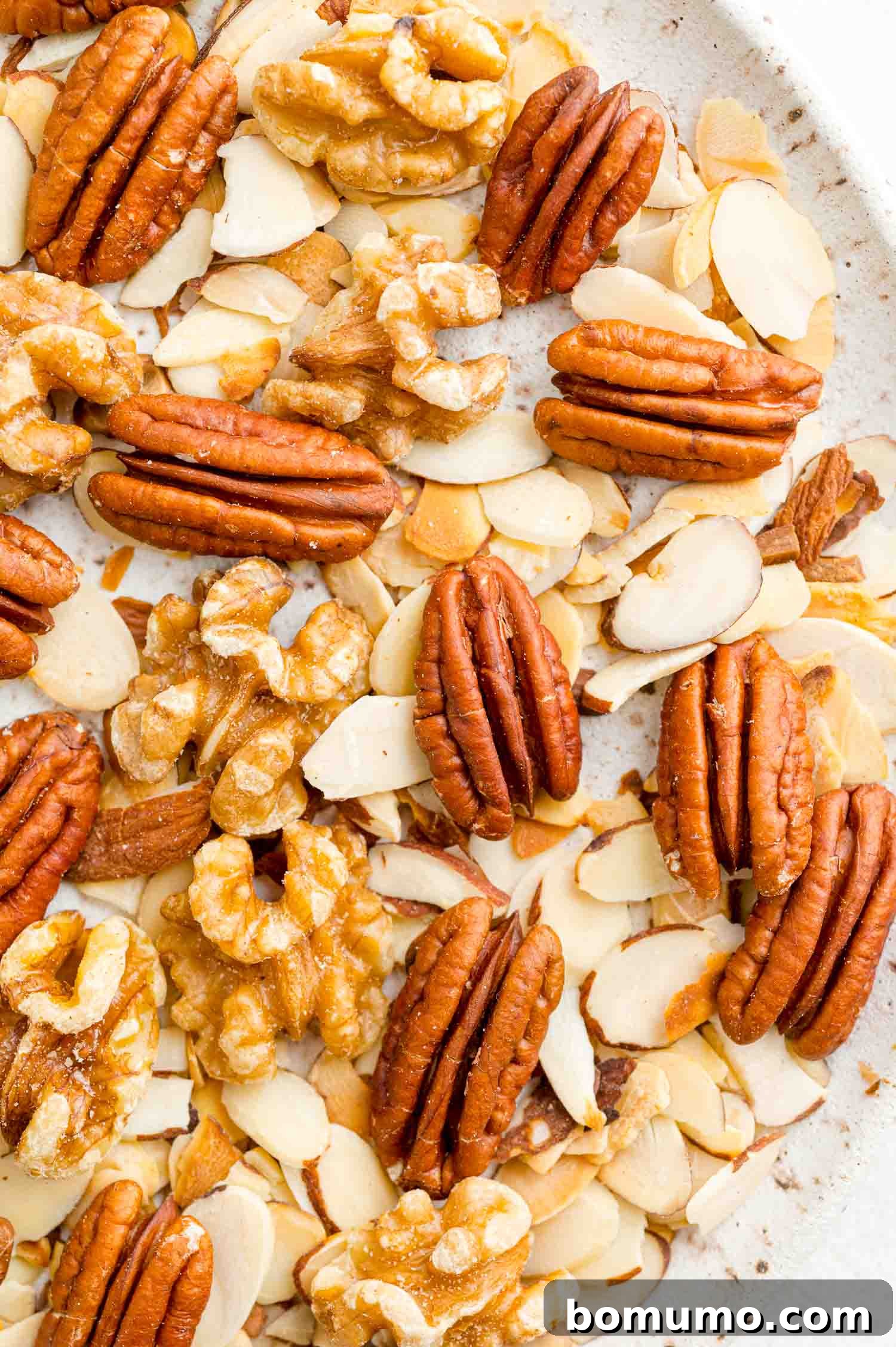 Toasting almonds is a great way to bring out their crunch and great flavor. Learn how to toast almonds in the oven, microwave, and on the stovetop! Close up of a medley of toasted almonds, walnuts, and pecans on a white plate.