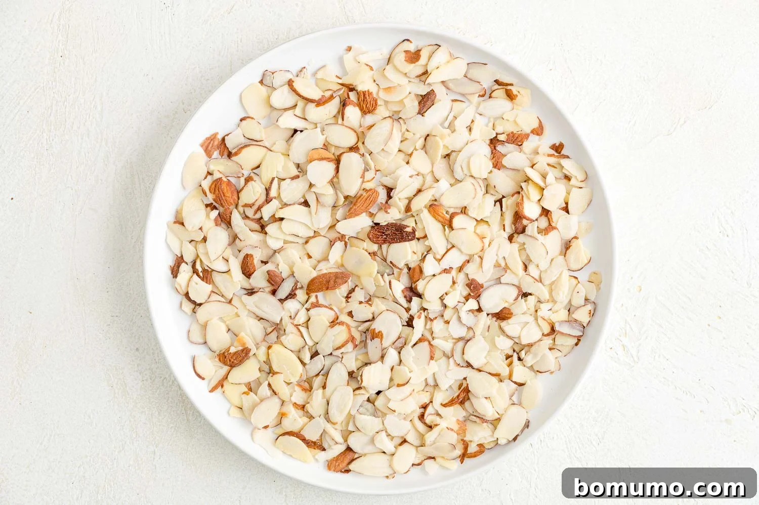 Toasting almonds is a great way to bring out their crunch and flavor. Learn how to toast almonds in the oven, microwave, and on the stovetop! Sliced almonds on a white plate.