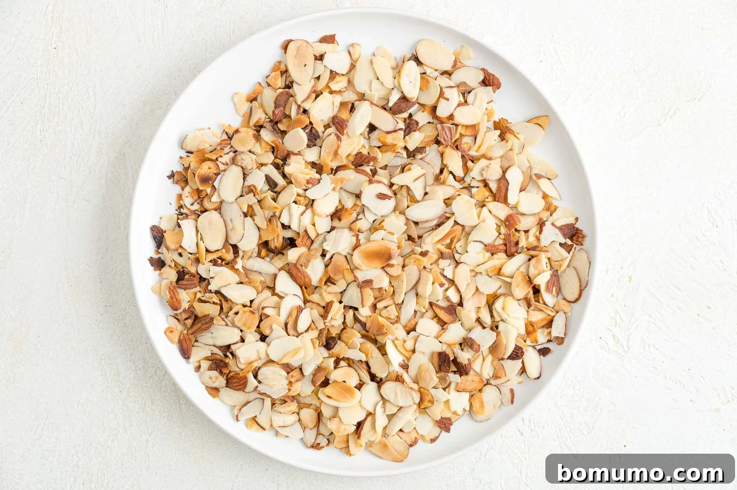 Toasting almonds is a great way to bring out their crunch and flavor. Learn how to toast almonds in the oven, microwave, and on the stovetop! Toasted almond slices on white plate.