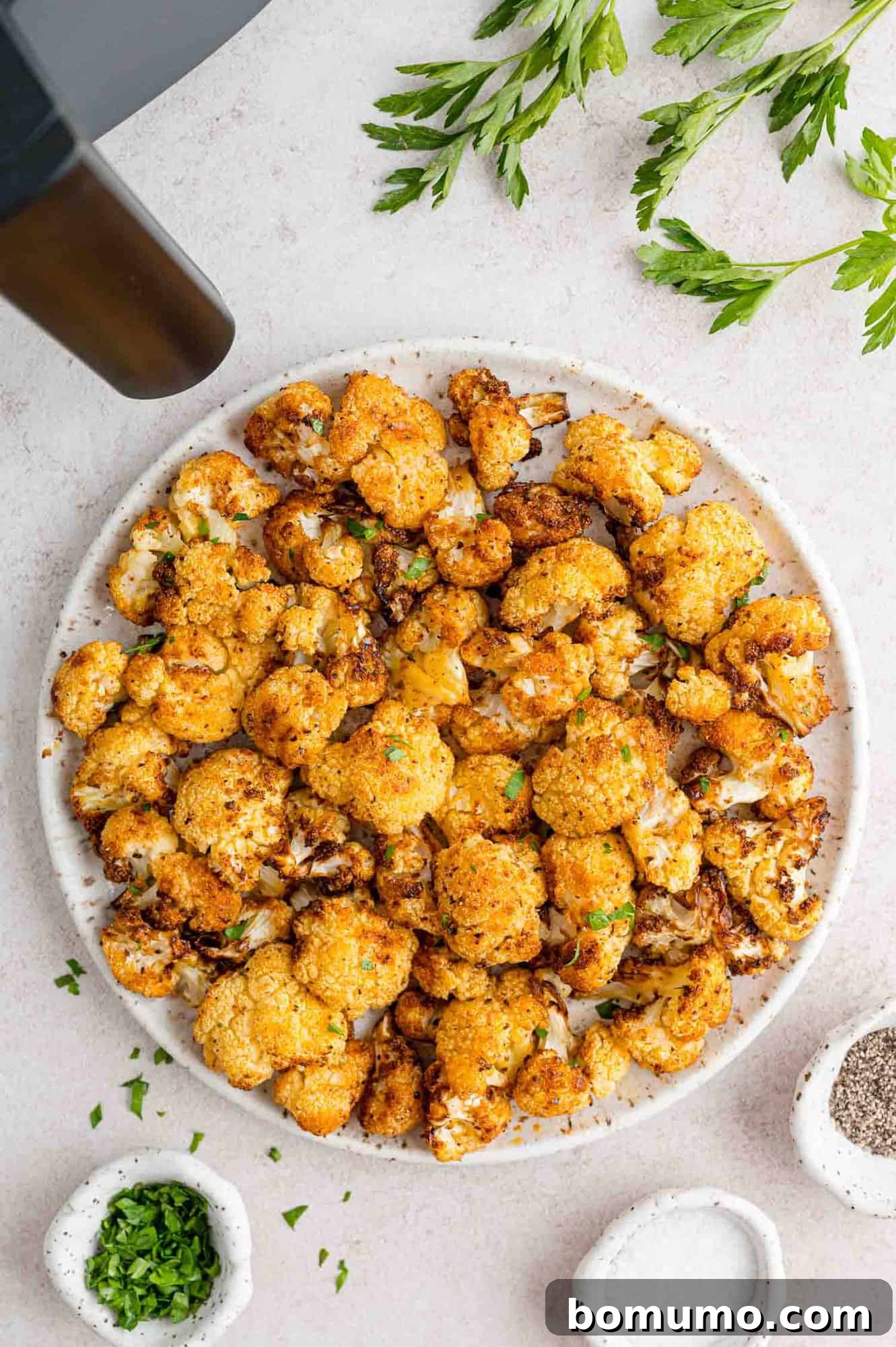 Overhead view of air fried cauliflower on a plate garnished with parsley, next to the air fryer.