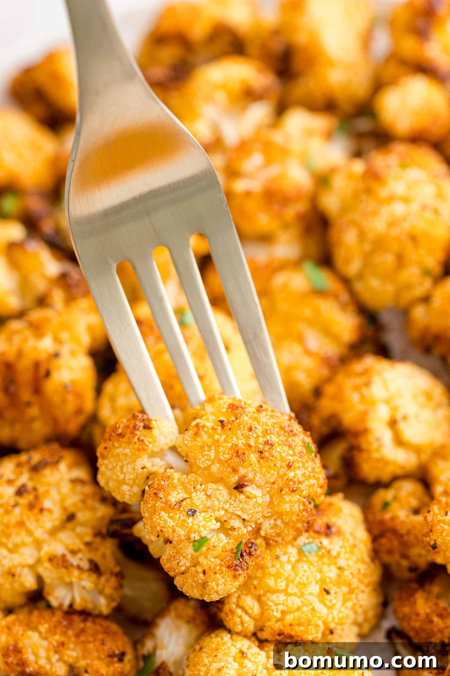 A fork stuck into a piece of air fried cauliflower.