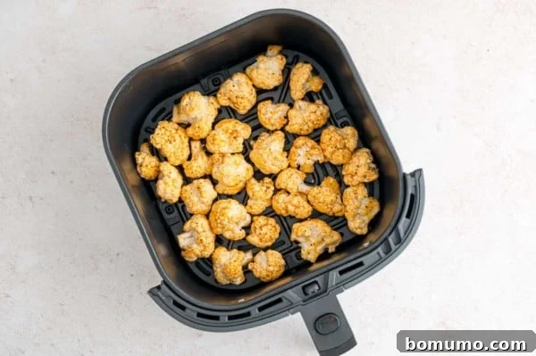 Seasoned uncooked cauliflower florets inside the air fryer basket.