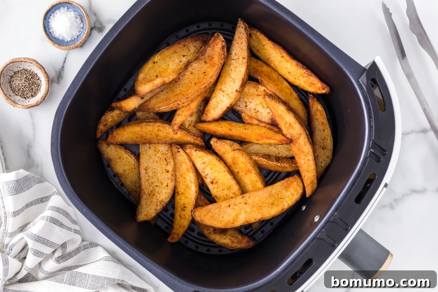 Perfectly cooked, golden brown and crispy potato wedges filling an air fryer basket.