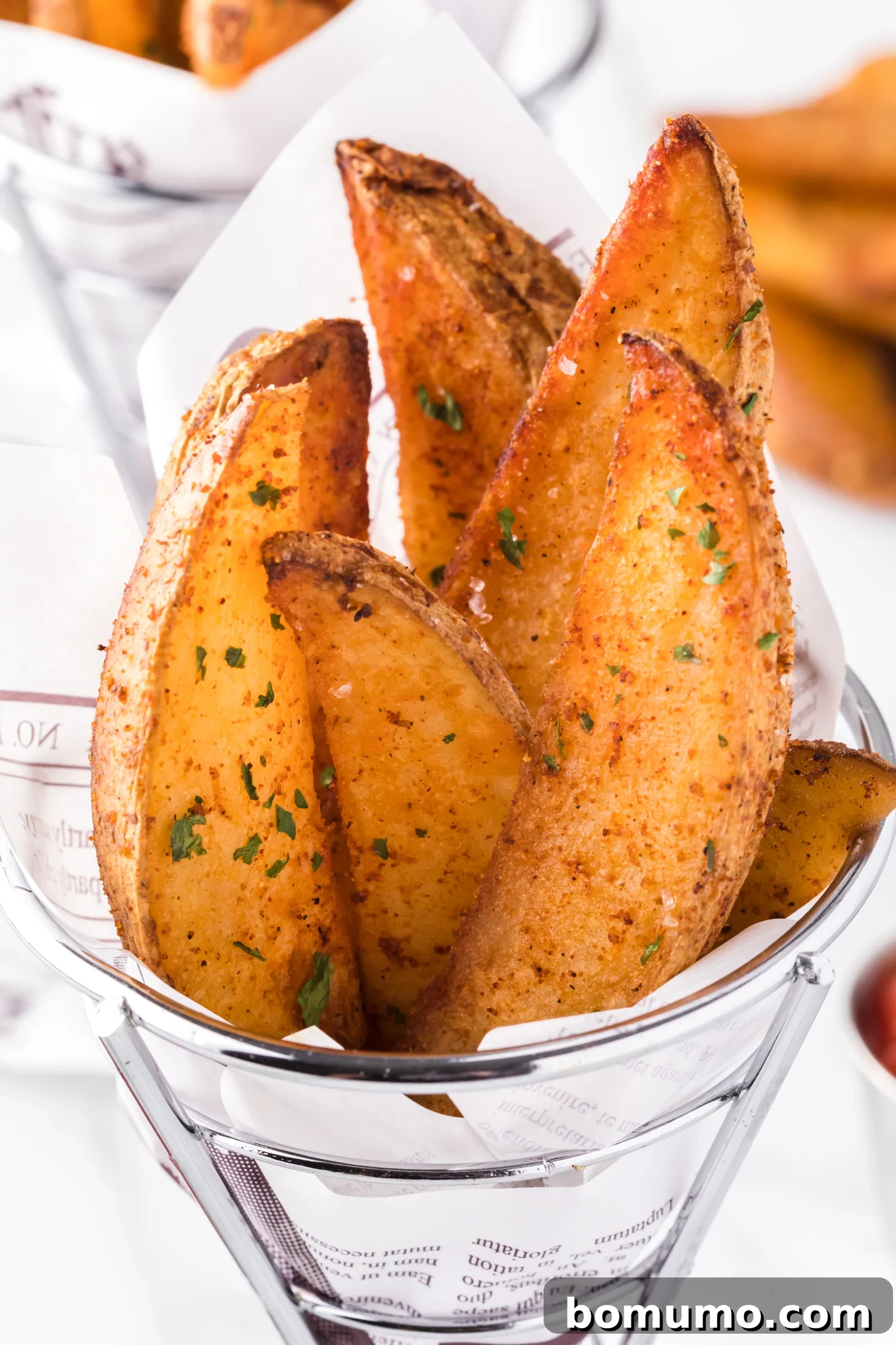 Crispy air fryer potato wedges served in a stylish cone-shaped basket, ready for dipping.